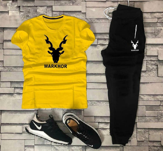Yellow t-shirt with 'MARKHOR' design, black pants, and black and white sneakers on a stone wall background.