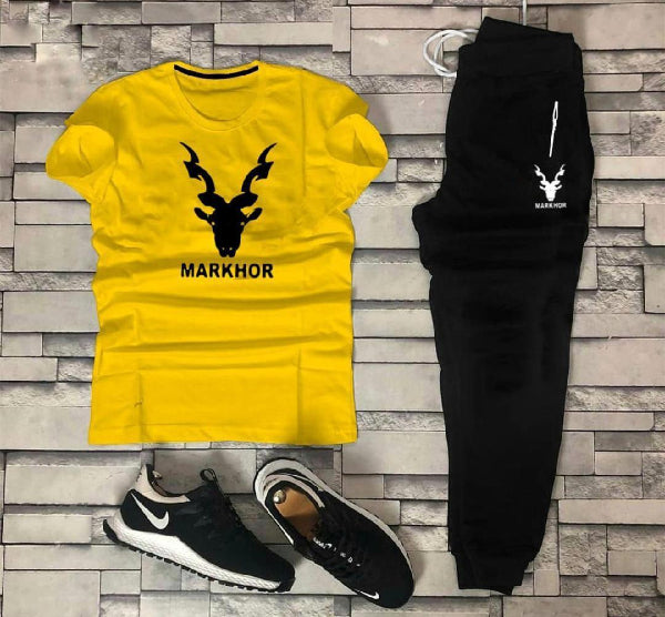 Yellow t-shirt with 'MARKHOR' design, black pants, and black and white sneakers on a stone wall background.